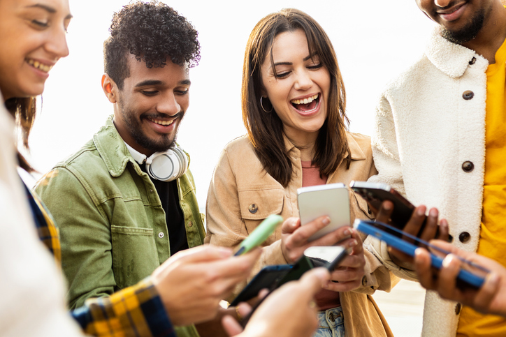 A group of people are gathered close looking at their smart phones together.