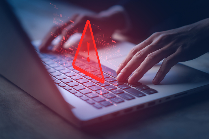 A red warning triangle hangs over a laptop. A website has been hacked.