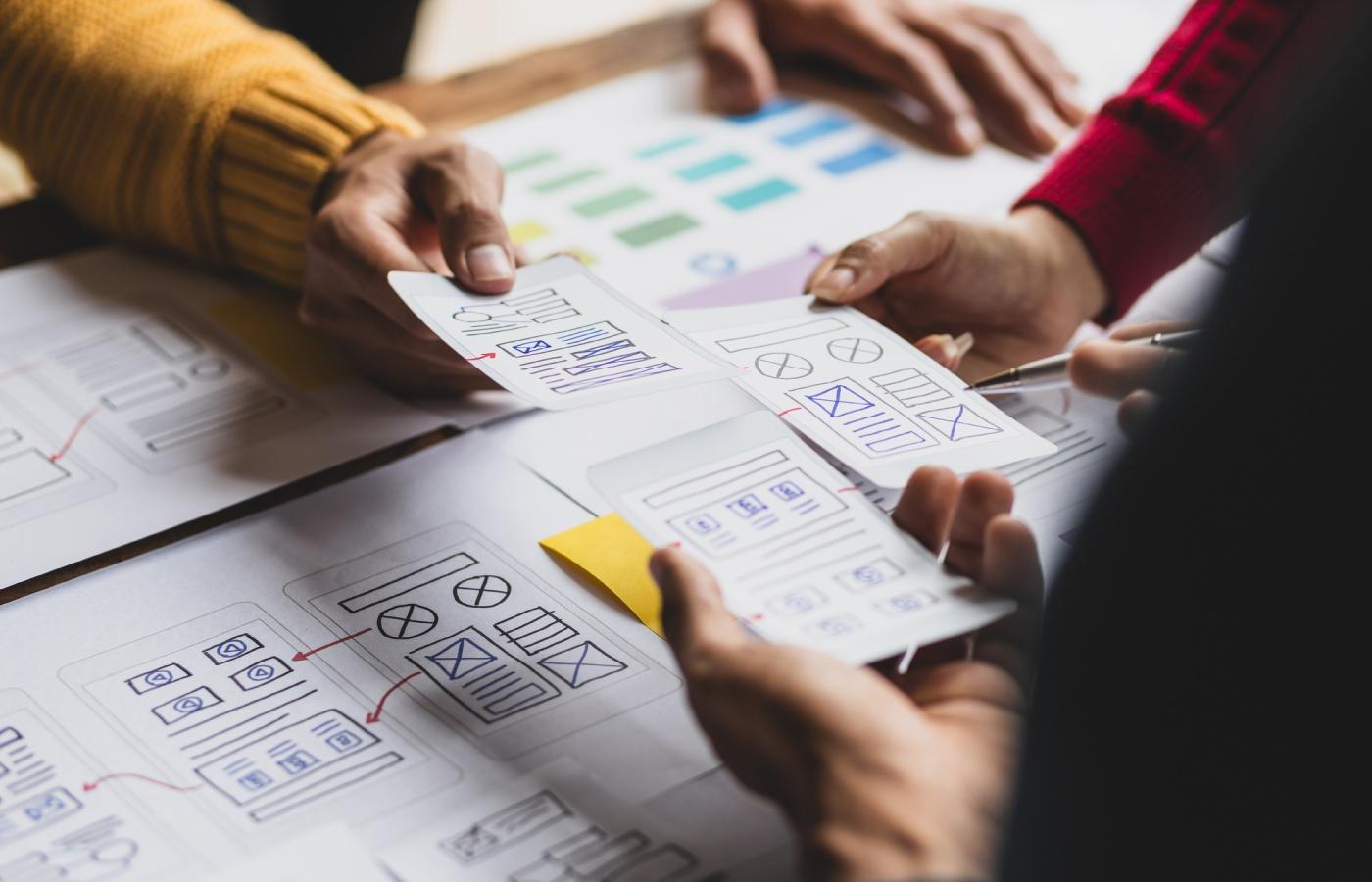 A group of designers collaborates on website navigation sketches, reviewing wireframes and layout elements on paper.