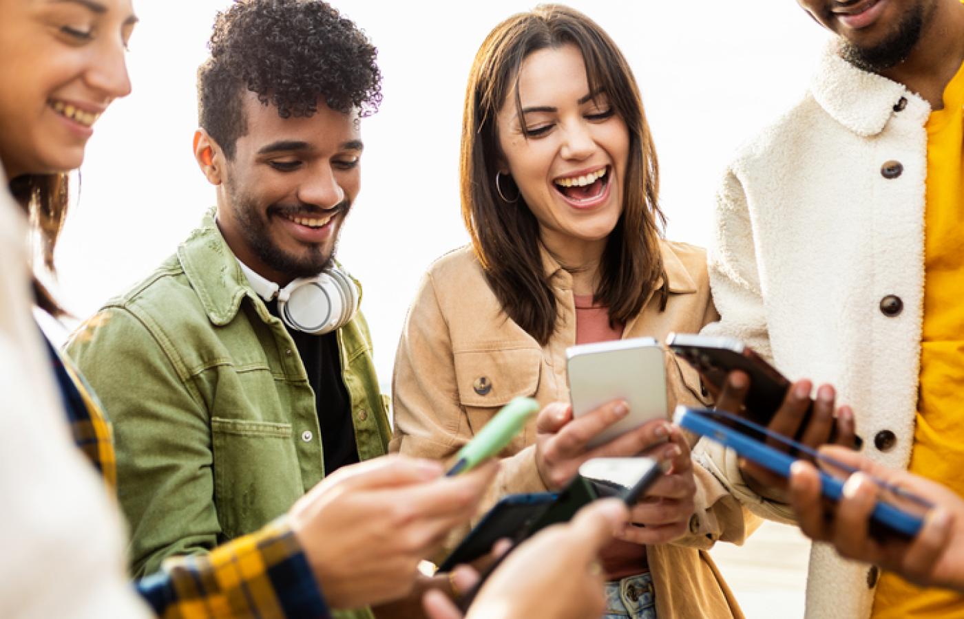 A group of people are gathered close looking at their smart phones together.