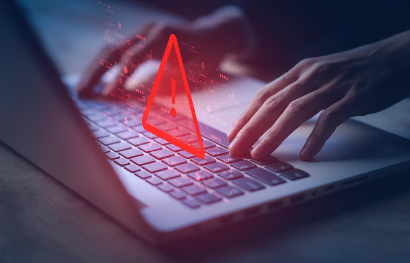 A red warning triangle hangs over a laptop. A website has been hacked.