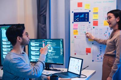Agile software team collaborating on code and visual planning board, showing sprint tasks and user flows.