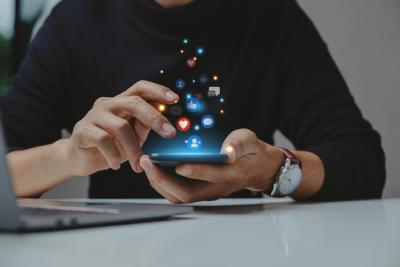Hands tapping on a mobile phone with social media icons glowing above the phone.
